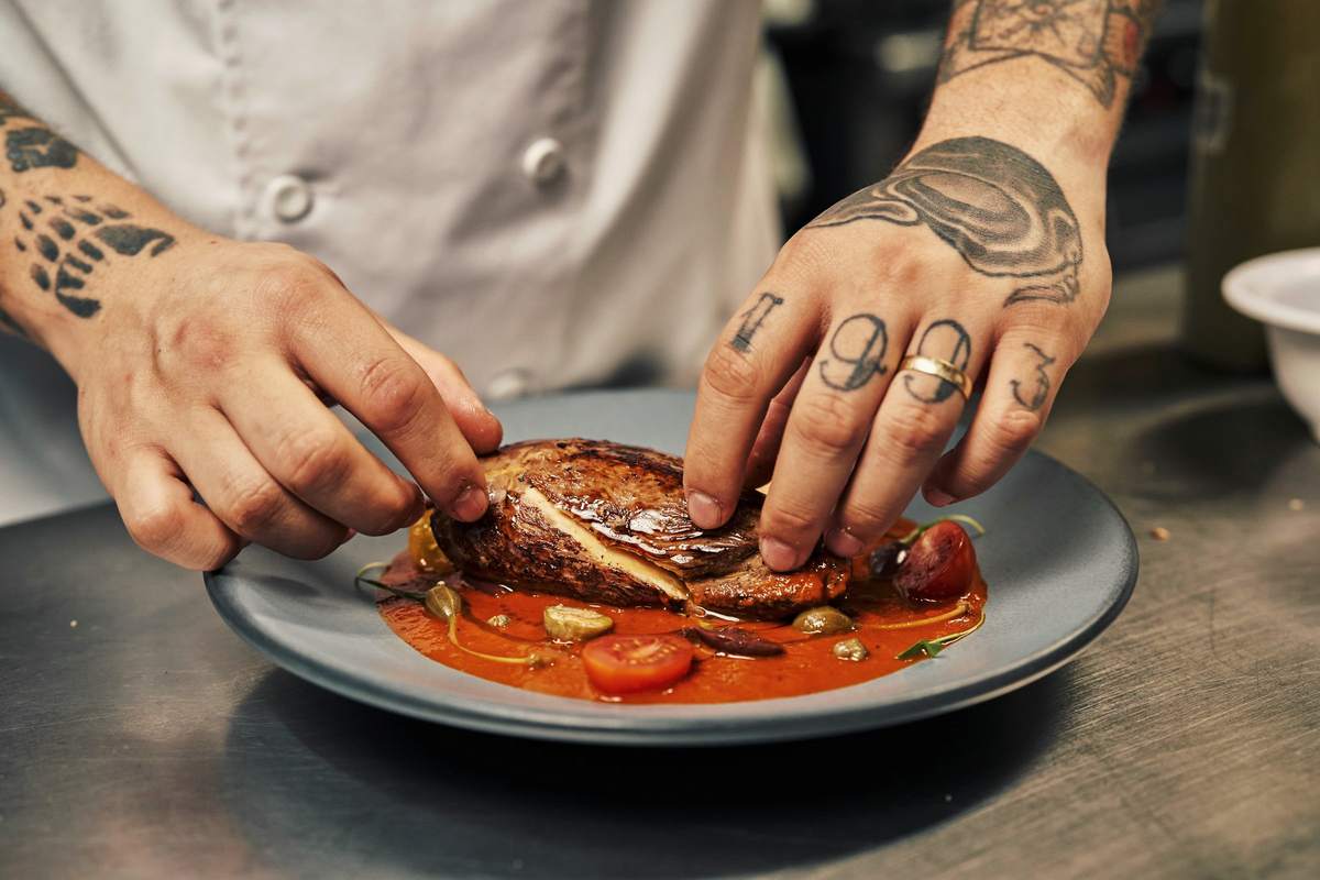 Hands plating a dish at the kitchen pass mid-service.