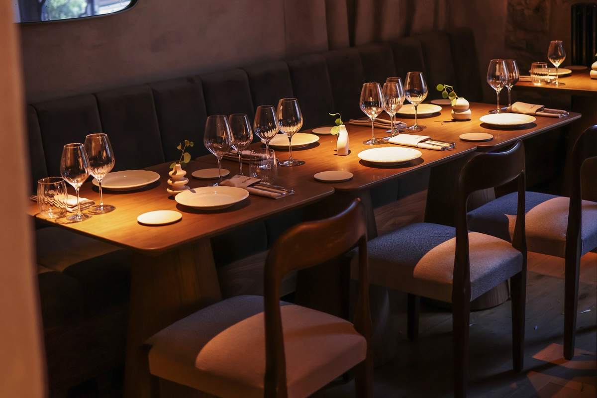 The dining room at Marrow: long tables under low light, set for the six o'clock.